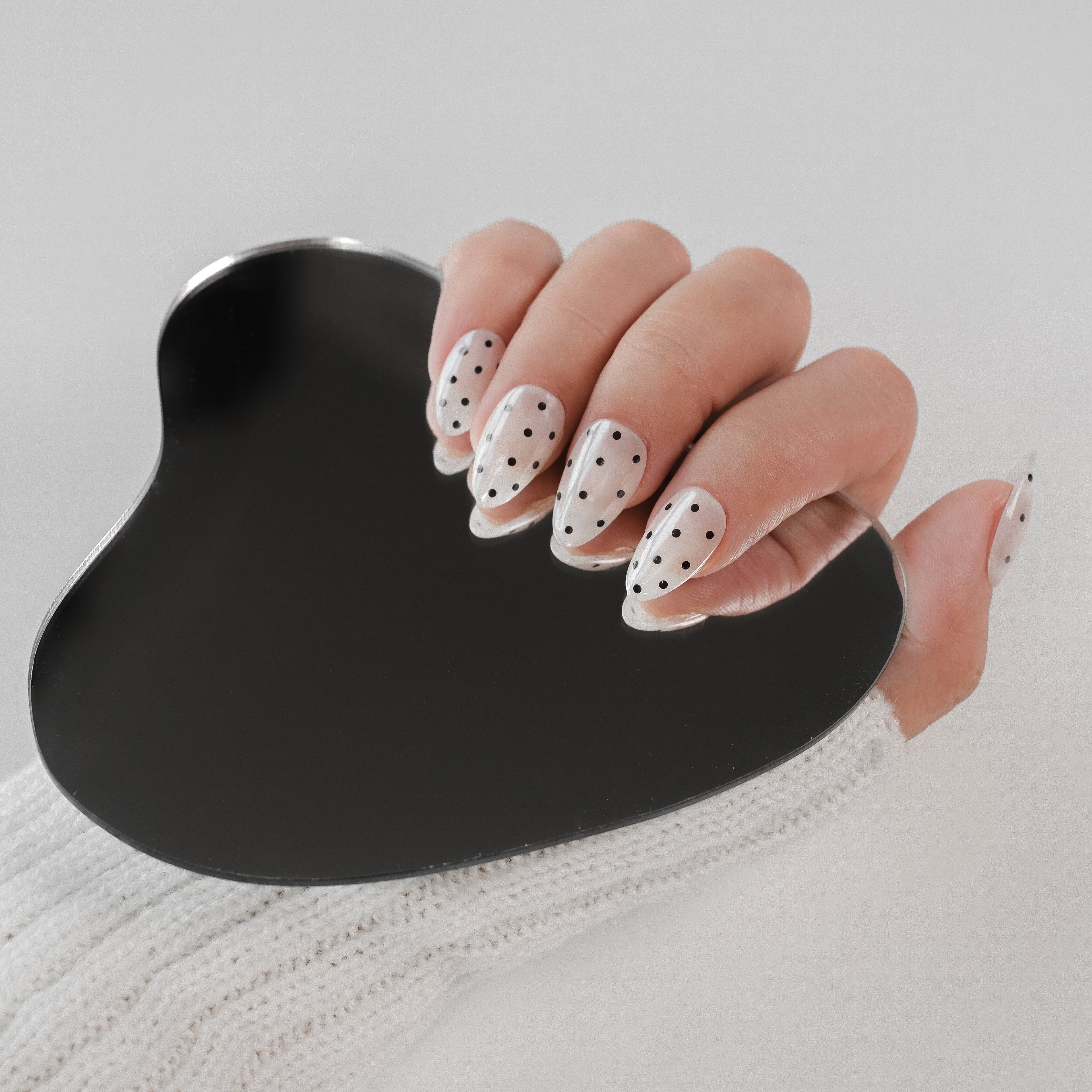 Handmade Nailique short almond press-on nails with chrome glaze, white and black polka dots, soft gel finish.