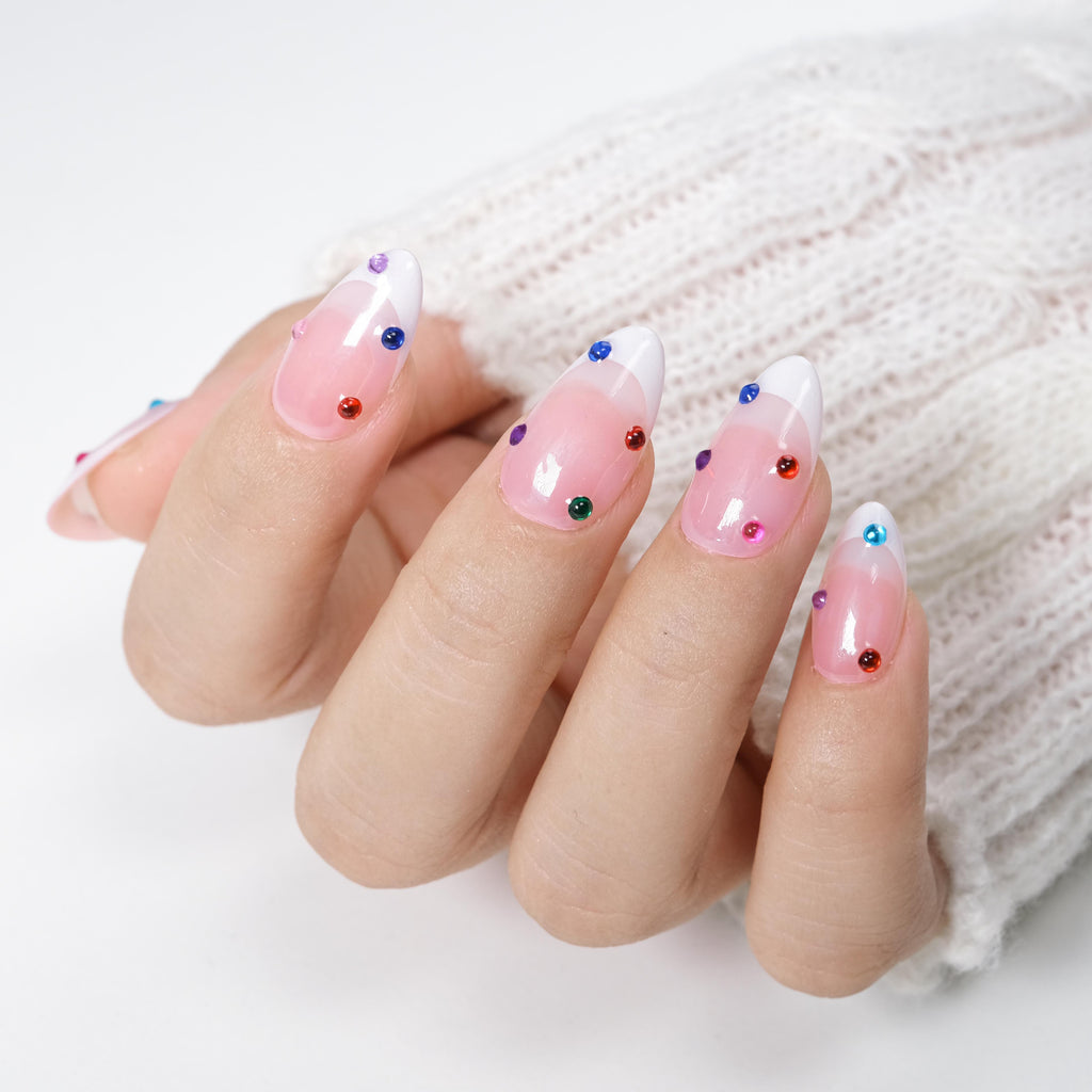 Short almond press-on nails by Nailique featuring nude color, white French tips, colorful rhinestones, and a sparkly gel finish.