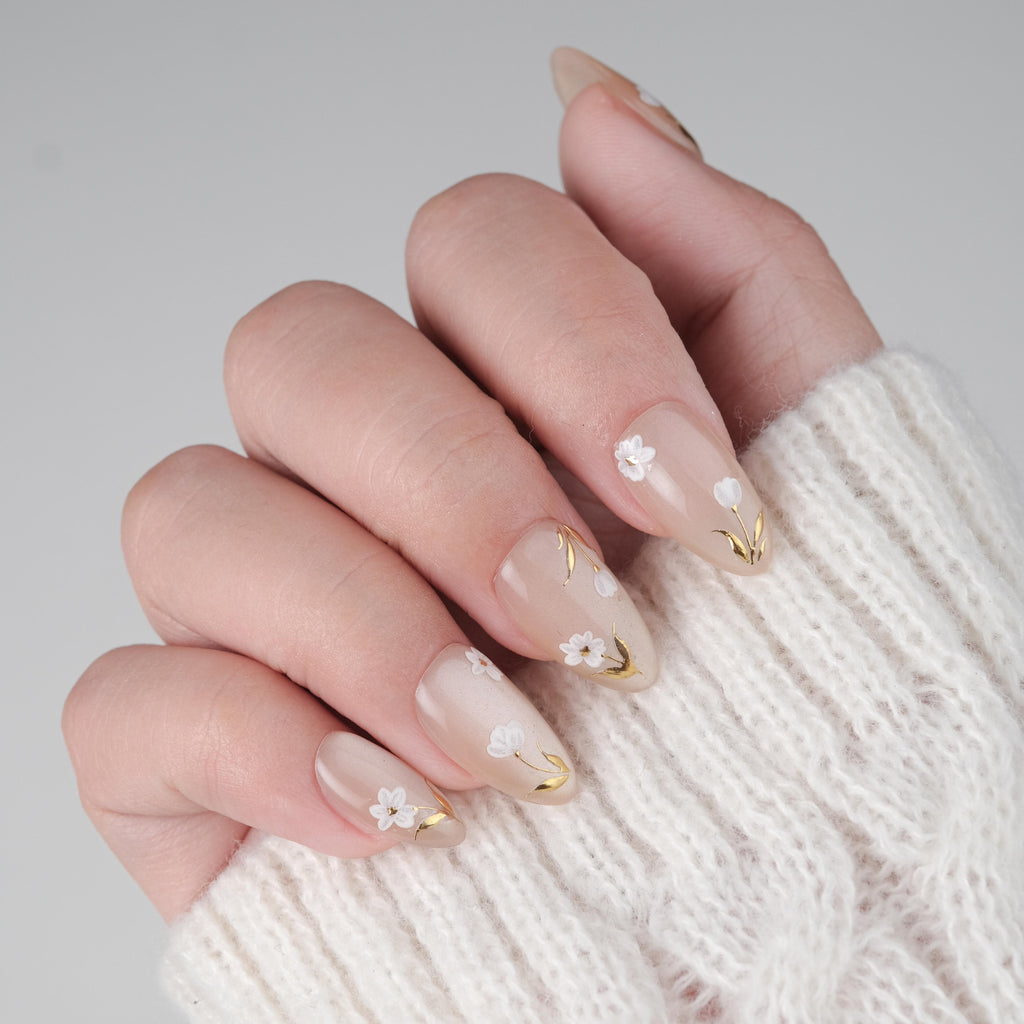 Handmade white floral short almond press on nails by Nailique with gold foil, reusable gel tips, and lamp-curable glue.
