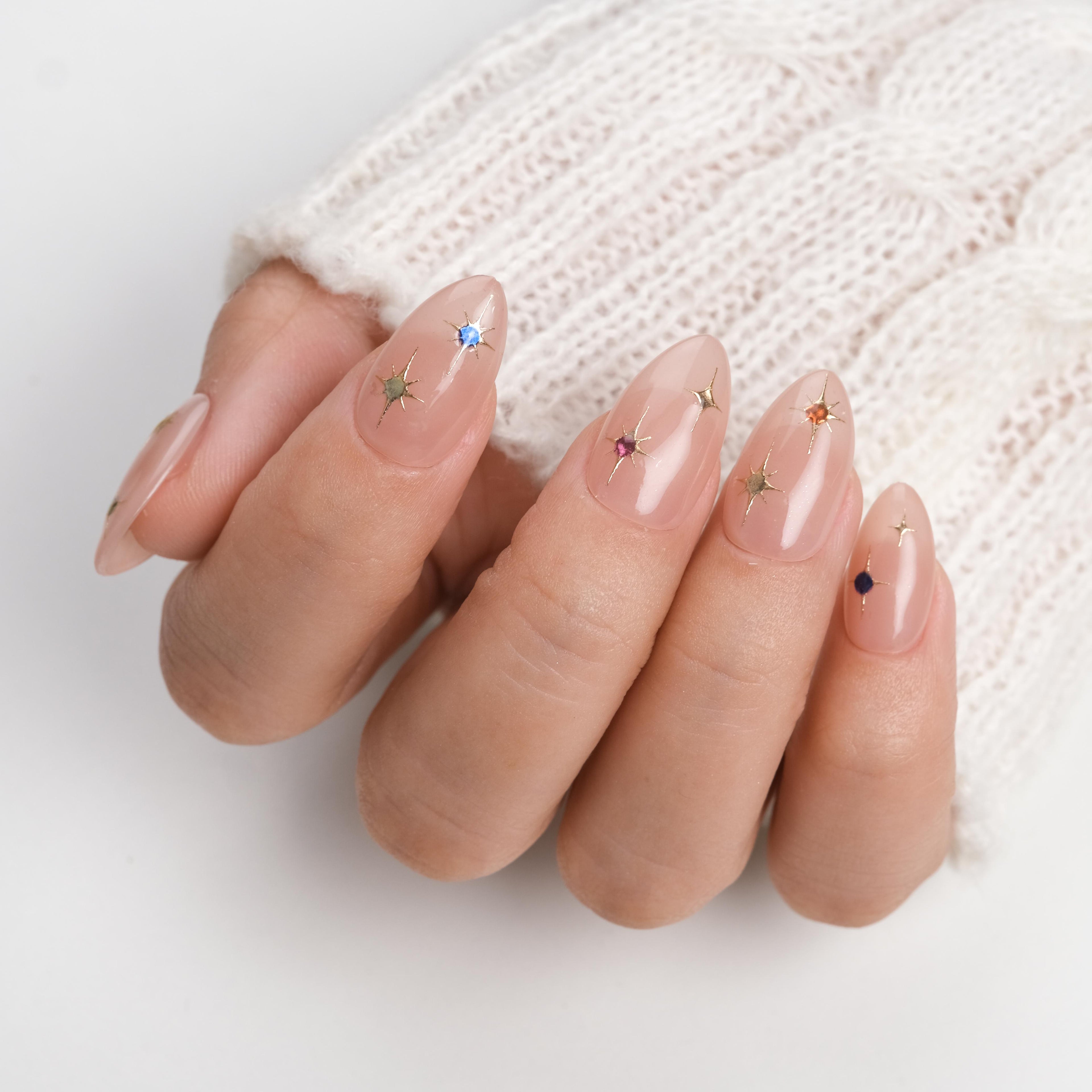 Short almond press-on nails by Nailique featuring soft nude pink gel tips with gold star accents and sparkling details.