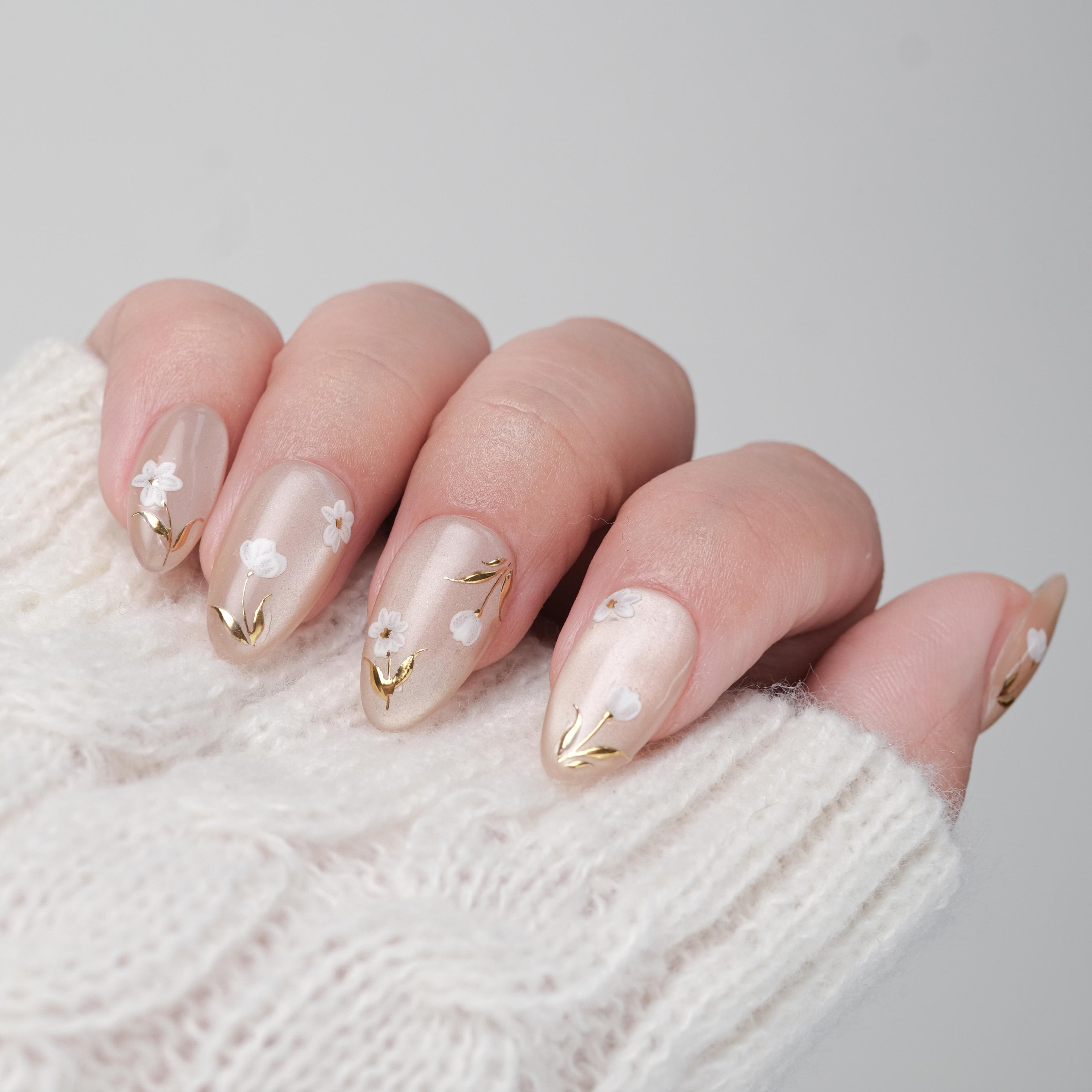 Short almond press on nails by nailique with white floral design, gold foil accents, reusable tips, and lamp-curable glue.