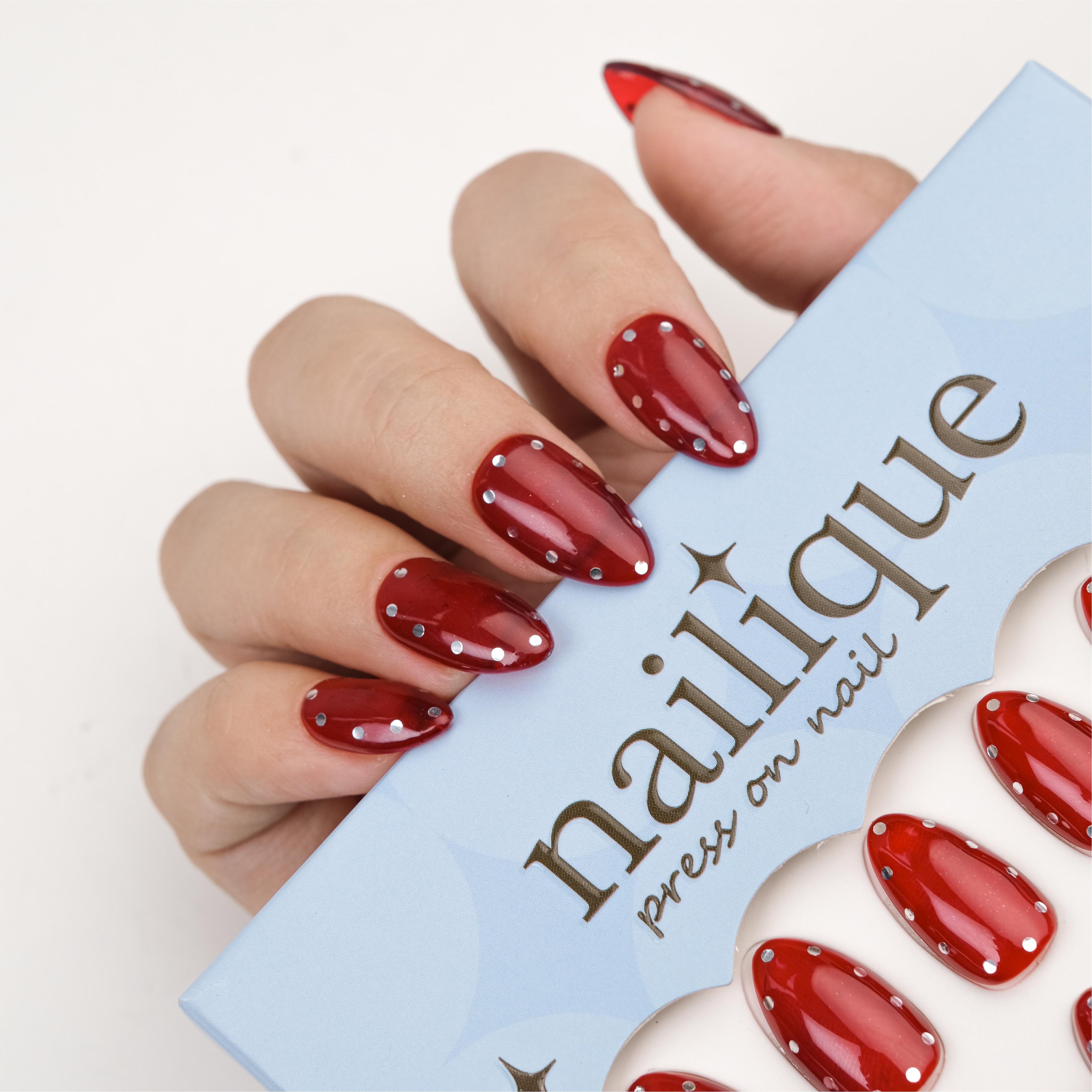 Short almond-shaped glossy red press-on nails with metallic studs, handmade gel polka dot manicure set by Nailique, 26 reusable tips.