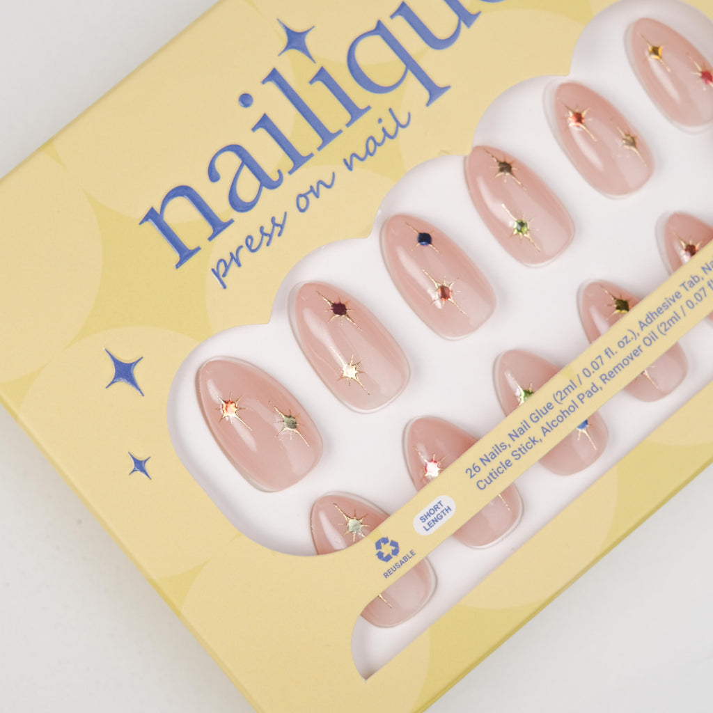 Short almond press-on nails by Nailique featuring soft nude pink gel finish, gold star accents, and colorful sparkle details.