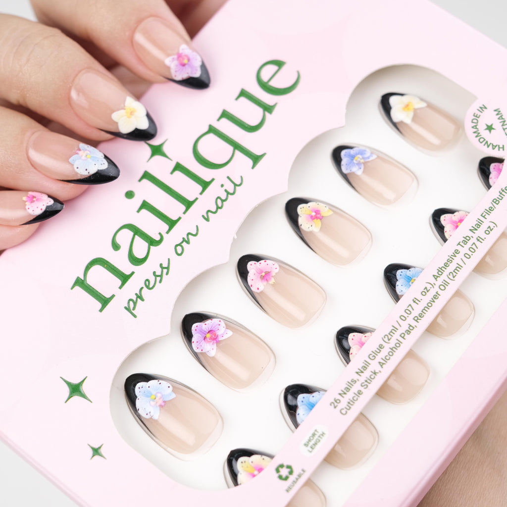 Short almond press-on nails by Nailique featuring black French tips and 3D orchid flower art in a set of 26 reusable gel fake nails.